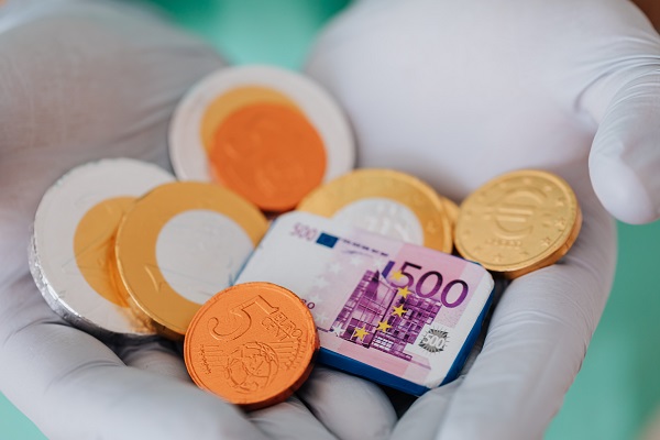 Zwei Hände, die medizinische Handschuhe tragen, zeigen Schokoladentaler in Form gäniger Euro-Münzen und einen 500-Euro-Schein.