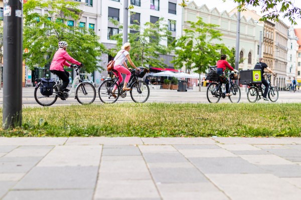 Radfahrerinnen und ein Radfahrer fahren entlang des Fahrradwegs auf dem Steintorplatz im Sommer